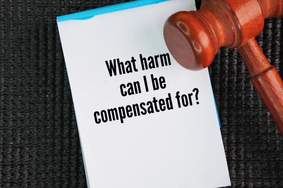 Gavel Beside a White Card with the Question 'what Harm Can I Be Compensated For?', on a Dark Carpet Surface.