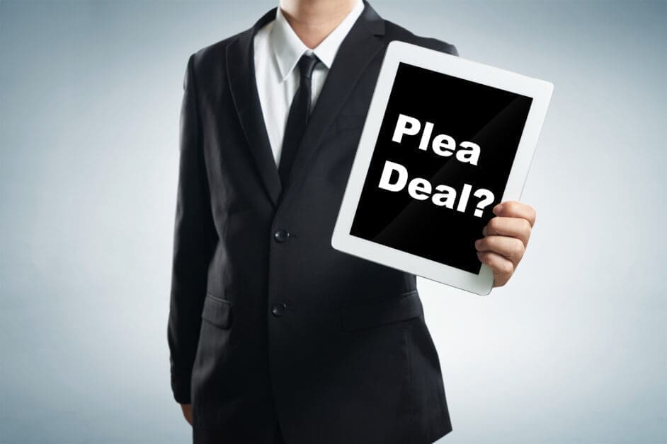 Suited Person Holding a Tablet Toward the Camera with the Words 'plea Deal?' On-screen