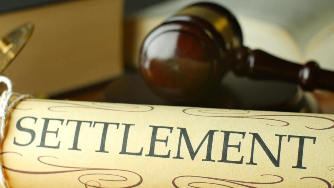 Close-up of a Rolled Document Labeled 'settlement' with a Wooden Gavel in the Background, Signaling Legal Resolution.
