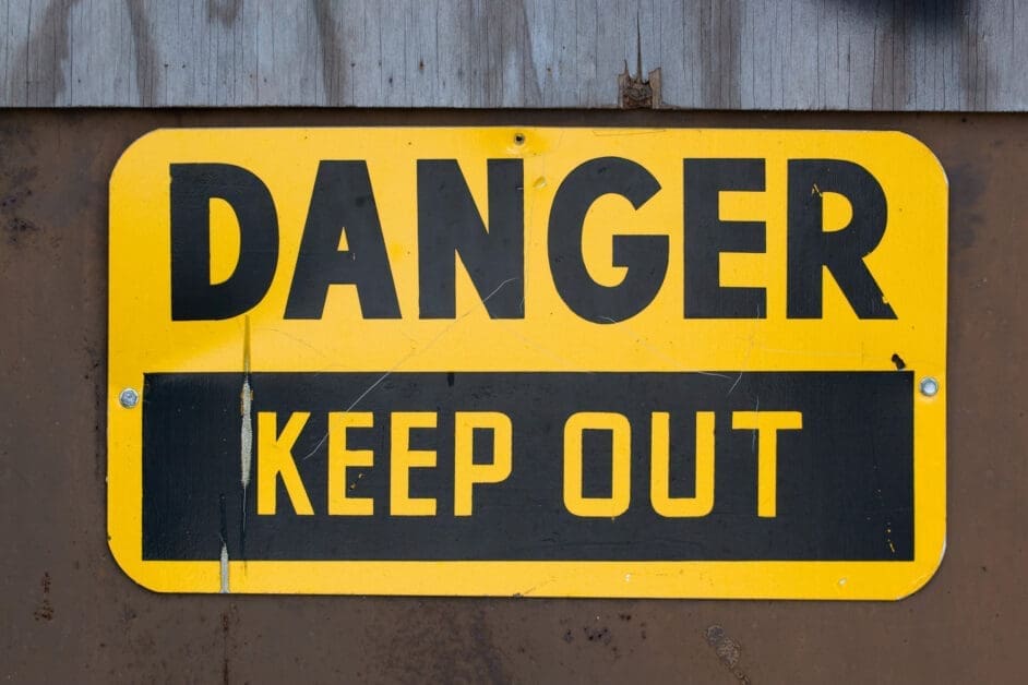 Large yellow danger sign with bold black 'DANGER' and a black panel reading 'KEEP OUT' on a weathered metal surface.