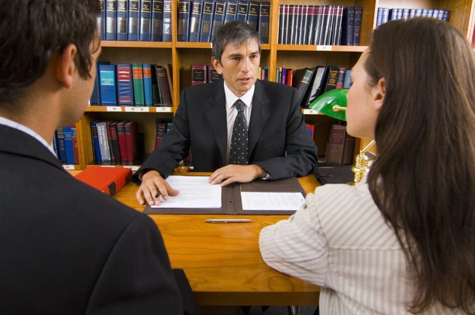 Attorney in a Black Suit Discusses Documents with a Man and a Woman in a Library-law Office Setting.
