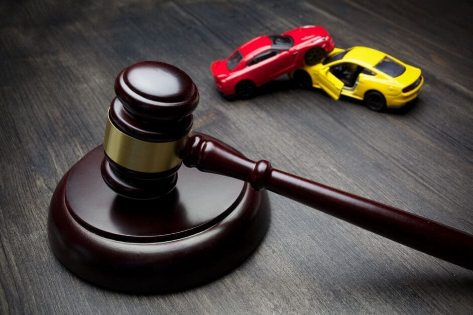 Judge's Gavel in Foreground with Red and Yellow Toy Cars in the Background on a Wooden Surface, Suggesting Traffic or Car-related Legal Proceedings.