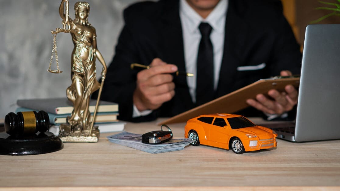Lawyer's Desk with the Scales of Justice, Gavel, Books, Money Stack, Key Fob, Orange Toy Car, and a Laptop in the Background.