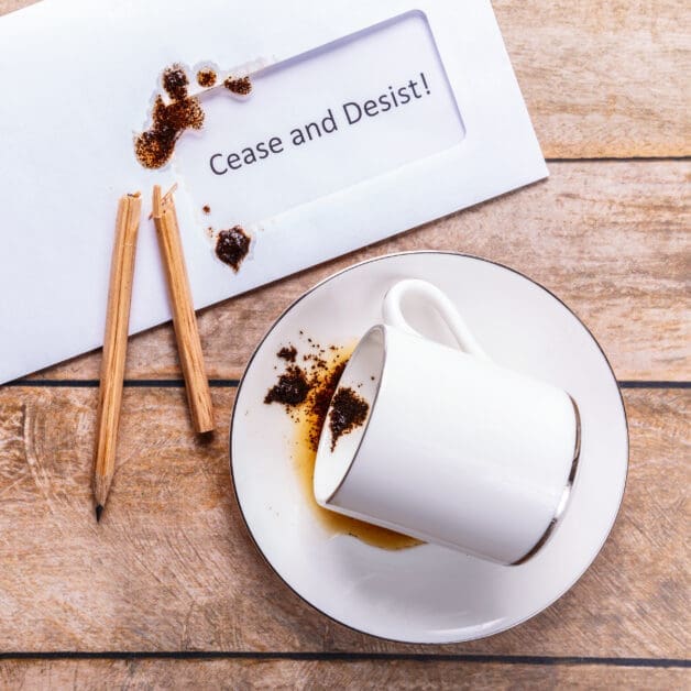 White Coffee Cup Tipped on a Saucer with Spilled Coffee and a Paper Note Reading 'cease and Desist!' Nearby
