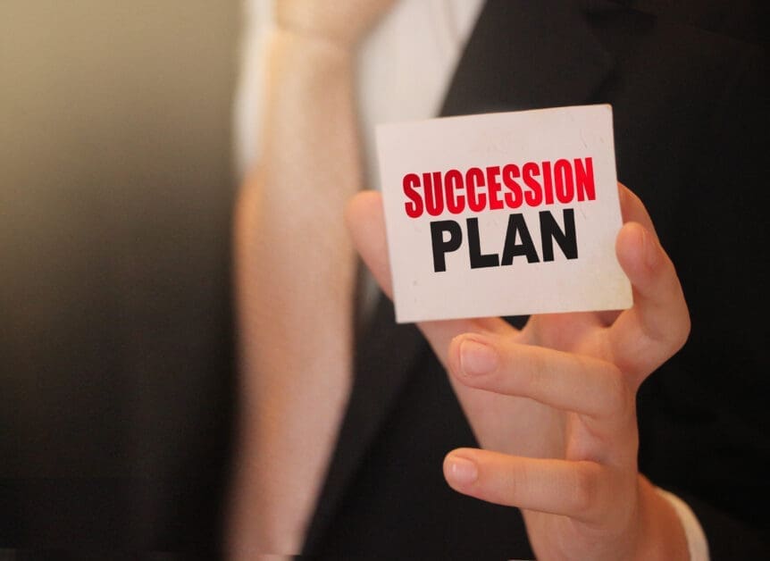 Close-up of a Person's Hands Holding a Card That Reads 'succession Plan' in Red and Black Letters.