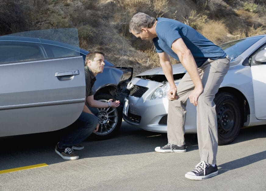 Two Men Kneel Beside Two Damaged Cars, Inspecting the Front Ends After a Collision on a Sunny Road.