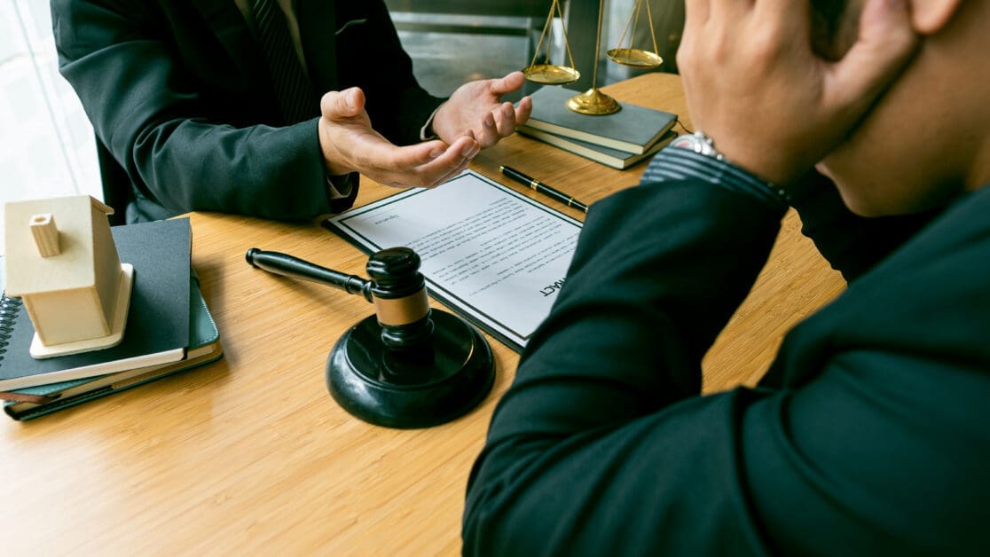 Two Professionals Discuss a Contract at a Wooden Table, with a Gavel, Scales, and Legal Books Nearby.