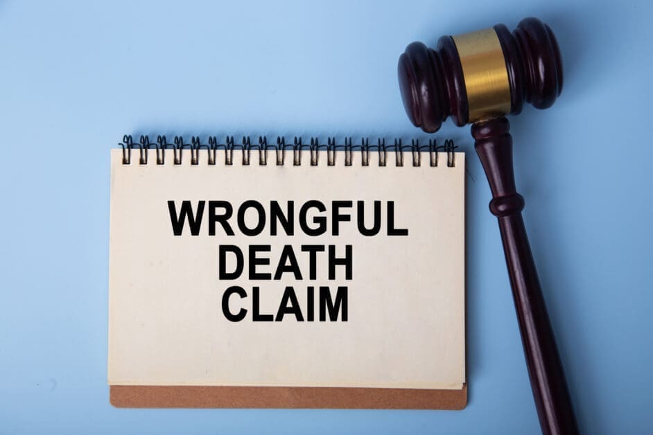 Notebook Page Reads 'wrongful Death Claim' Beside a Judge's Gavel on a Blue Background, Conveying Legal Action Context.