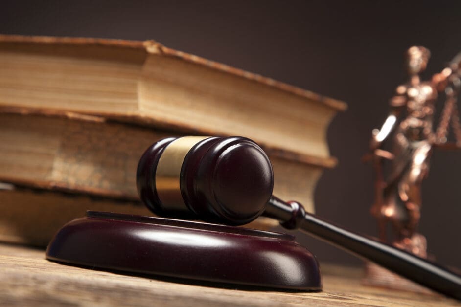 Gavel Resting on a Wooden Desk with Old Law Books in the Background for Context of a Legal Setting.