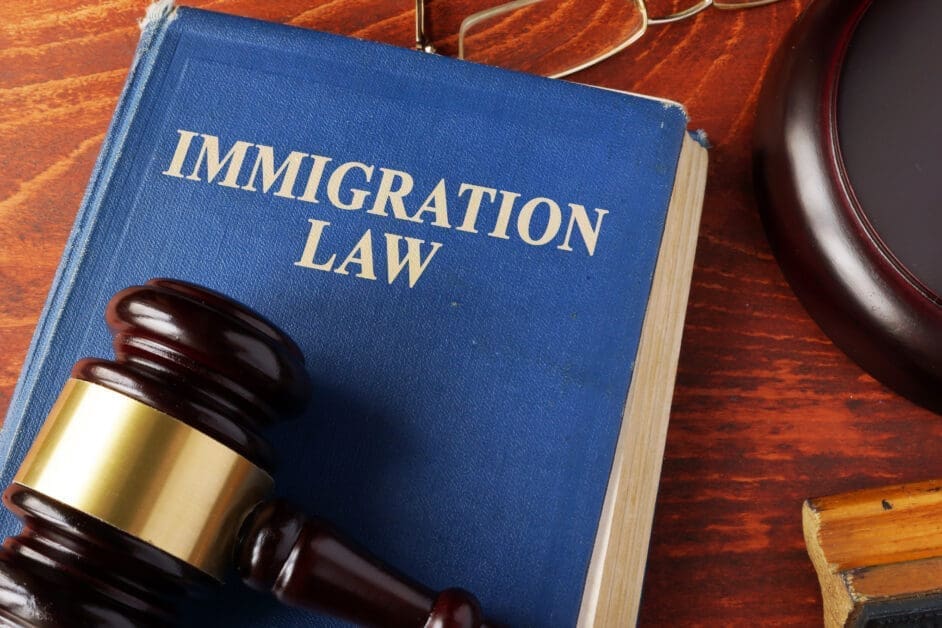 Blue immigration law book with a gavel resting on a wooden desk surface.