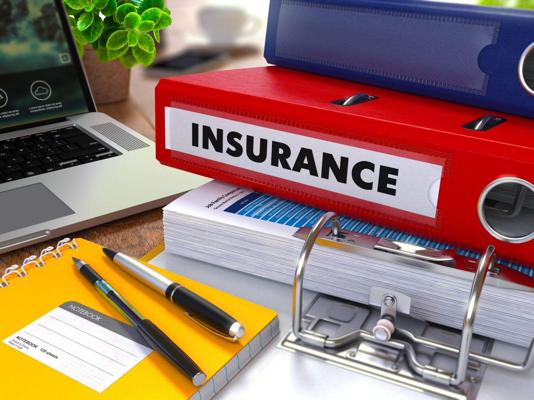Red Insurance Binder Labeled Insurance on a Desk Beside a Laptop and Office Supplies.