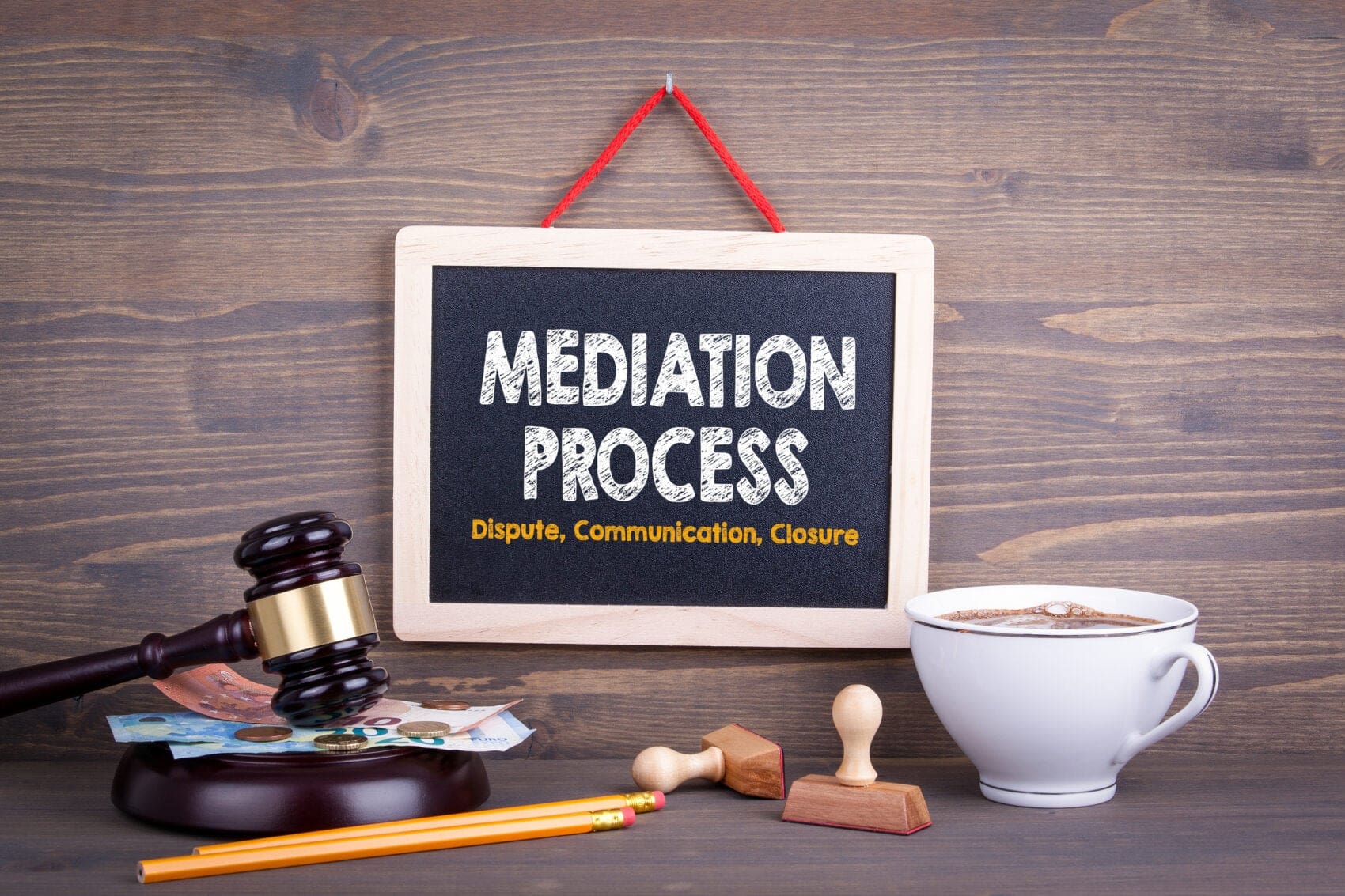 Signboard Reads 'mediation Process' with Subtitle 'dispute, Communication, Closure' on a Wooden Background; Includes Gavel, Money, Coffee Cup and Desk Items Nearby.
