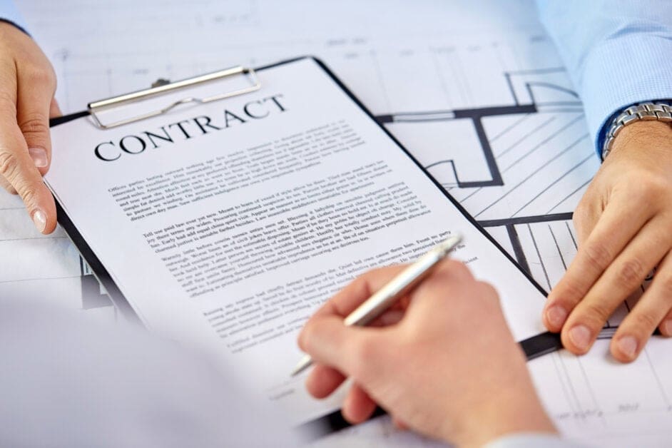Two Hands Hold a Clipboard with a Contract; a Pen Signs the Document over a Blueprint Background, Suggesting a Business Agreement.