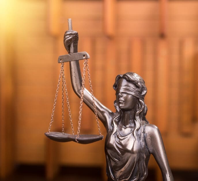 - Attorneys.Media - Legal Expert Interviews & Trusted Advice Bronze Statue of Lady Justice Holding a Balance Scale Against a Warm, Blurred Background.