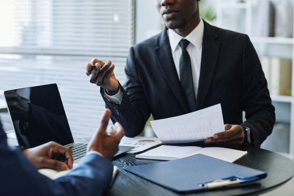 Business Partners in Meeting - Attorneys.Media - Legal Expert Interviews & Trusted Advice Two Professionals in Suits at a Conference Table, Exchanging a Document with Charts Beside a Laptop.